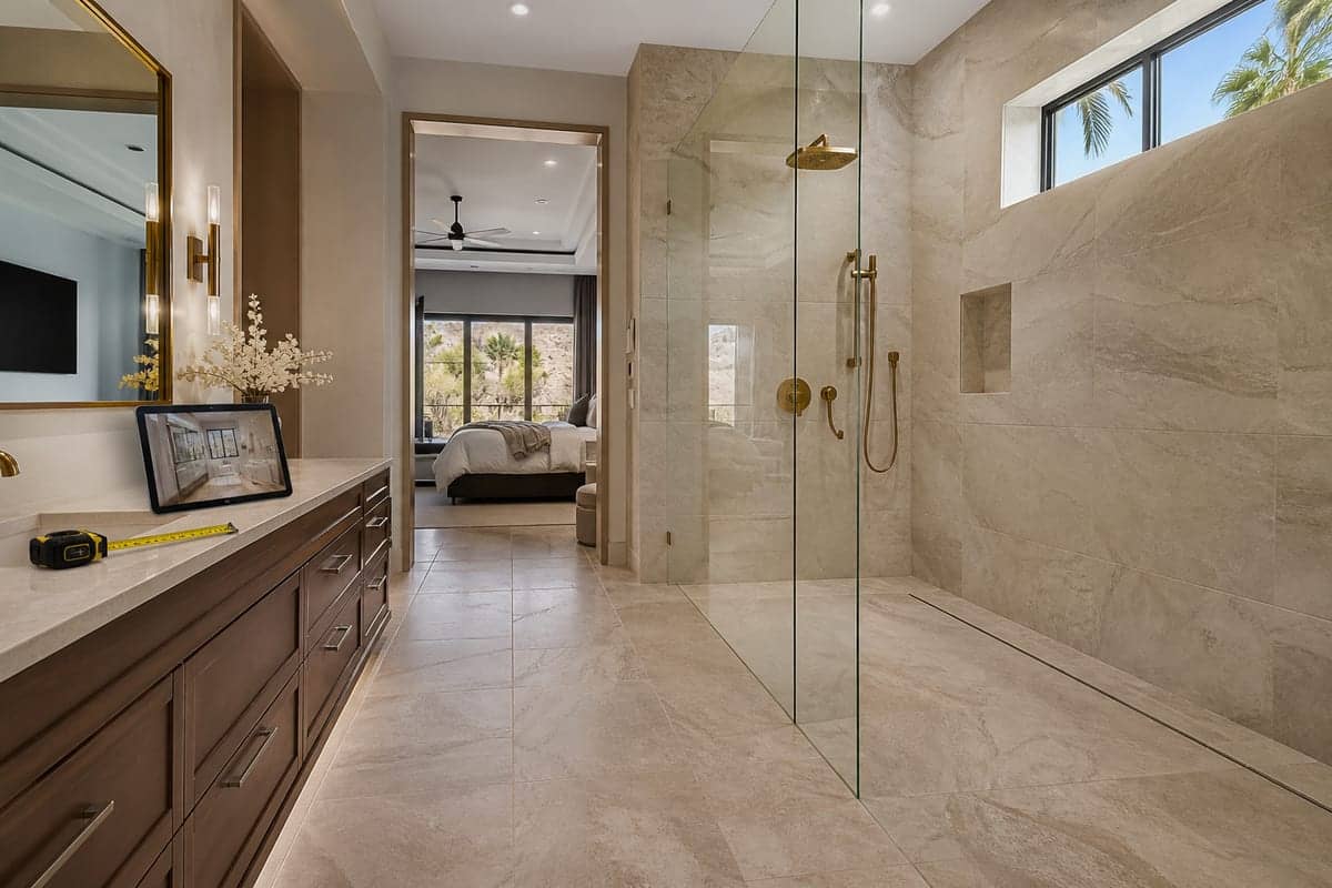 Residential curbless shower with a linear drain, brass fixtures, and a tablet showing the same bath on Zoom.