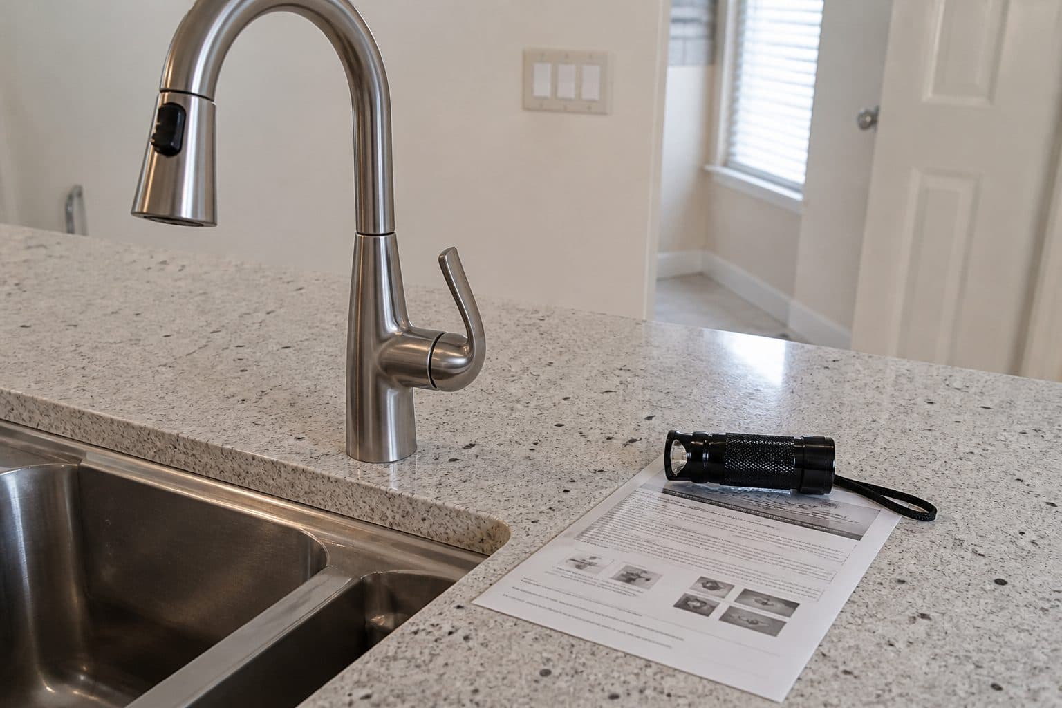 Inspection flashlight and an access checklist on a kitchen counter beside a lever faucet.